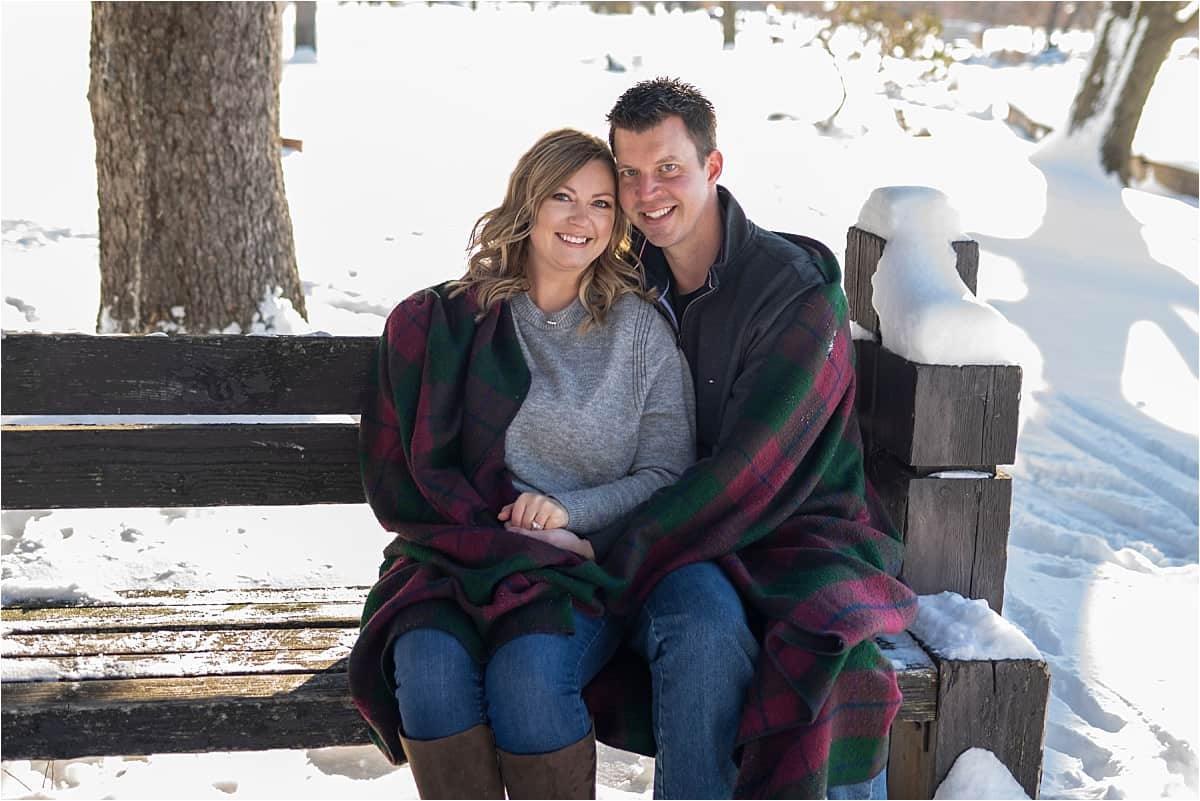 engaged couple wrapped in a blanket on a bench