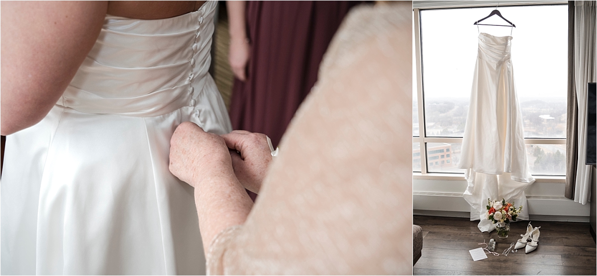 Mother buttons bride's dress and wedding dress hanging in front of window